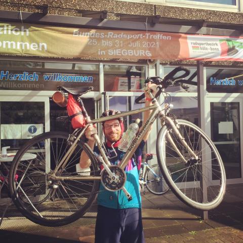 Andi hebt sein Rad hoch, im Hintergrund das Banner des Bundes-Radsport-Treffs